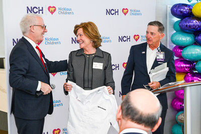 Nicklaus Children’s Health System President and CEO, Matthew A. Love (left) and NCH President and CEO, Paul Hiltz (right), gift Julia Van Domelen (middle) an honorary white coat.